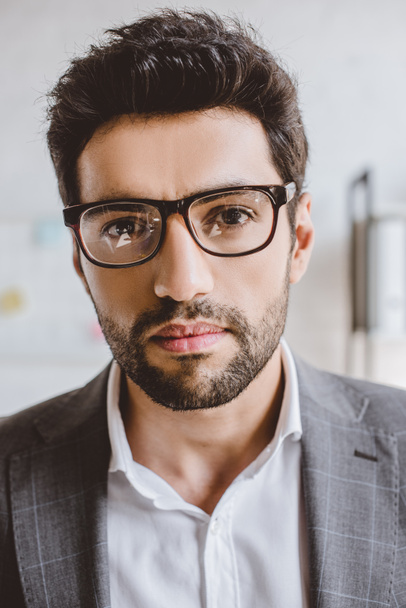 portrait of handsome businessman with bristle in glasses looking at camera in office  - Photo, Image