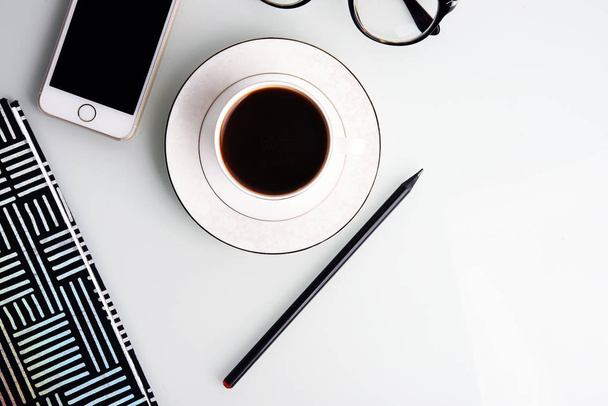 Office desk with coffee cup, pencil, smartphone, eyeglasses and striped notepad - Photo, Image