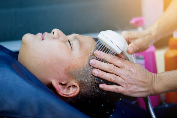 Un salon de coiffure. Coiffeur laver les cheveux à un garçon asiatique avec shampooing et
 - Photo, image