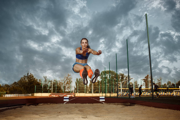 Female athlete performing a long jump during a competition - Φωτογραφία, εικόνα