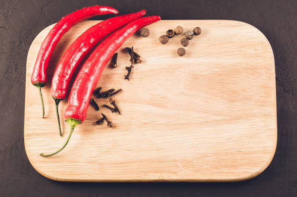Red hot chili peppers and spices on a empty cutting board/Red hot chili peppers and spices on a empty cutting board on a dark background. Top view - Photo, image