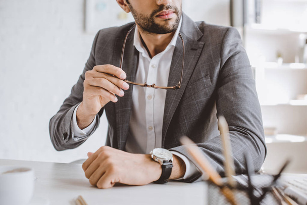 cropped image of businessman holding glasses at table in office - Foto, afbeelding