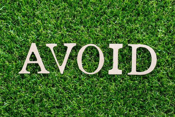 Деревянная буква в слове избежать на искусственном зеленом фоне травы
 - Фото, изображение