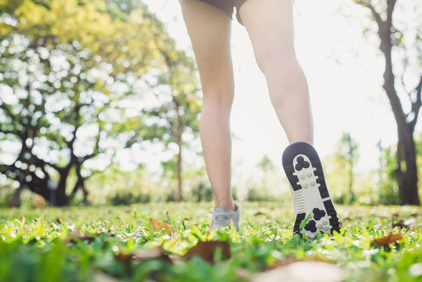 Nahaufnahme der Beine einer jungen Frau beim Aufwärmen des Körpers, indem sie ihre Beine vor Morgengymnastik und Yoga im Gras unter warmem Licht dehnt. Bewegungskonzept im Freien. - Foto, Bild