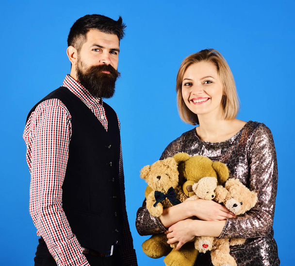 Girl and bearded man with happy faces play with soft toys. Couple in love holds heap of teddy bears on blue - Valokuva, kuva