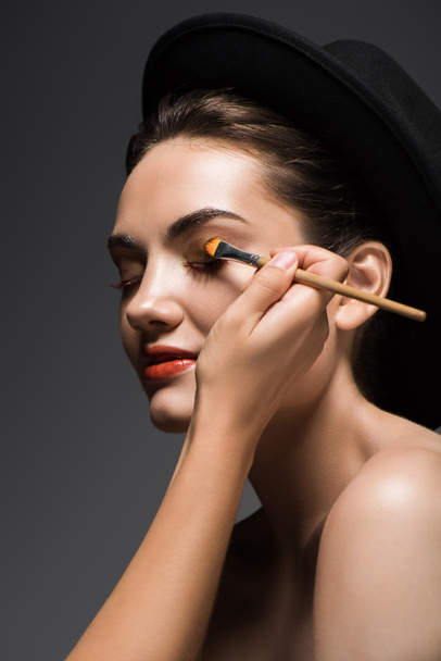 schoonheidsspecialiste eyeshadows toe te passen op meisjes gezicht met cosmetische penseel, geïsoleerd op grijs - Foto, afbeelding