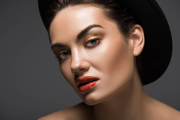 elegant model with makeup posing in stylish felt hat, isolated on grey - Photo, Image