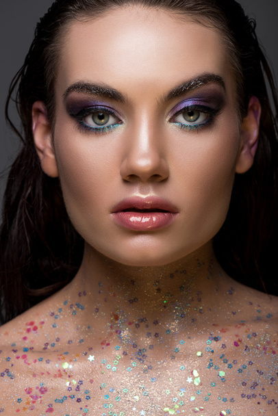 beautiful glamorous girl posing with glitter on body and looking at camera, isolated on grey - 写真・画像