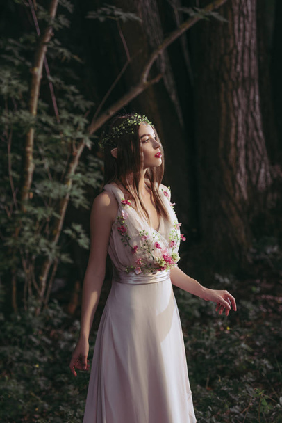 attractive mystic elf in dress with flowers in dark woods - Фото, зображення