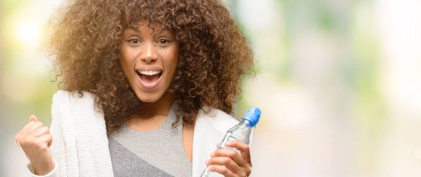 Afroamericana fitness mujer sosteniendo botella de agua gritando orgulloso y celebrando la victoria y el éxito muy emocionado, animando emoción
 - Foto, Imagen