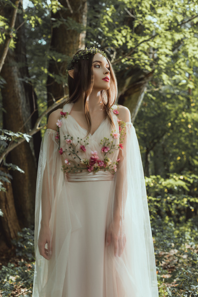 attractive mystic elf in floral wreath and dress with flowers in woods - 写真・画像