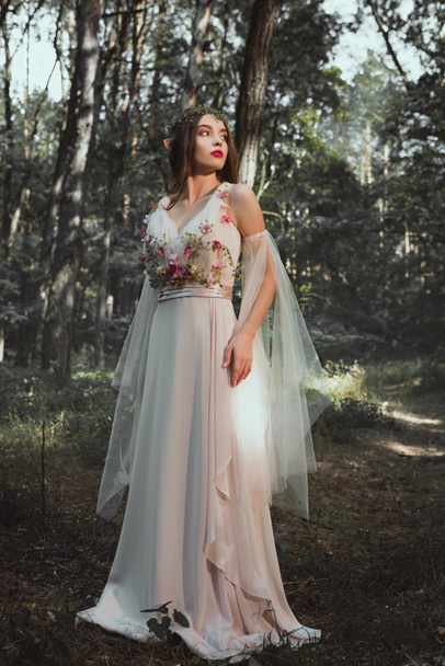 elf character in flower dress and wreath posing in forest - Photo, Image