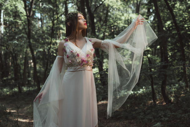 beautiful elf in elegant dress with flowers posing in forest - Фото, зображення