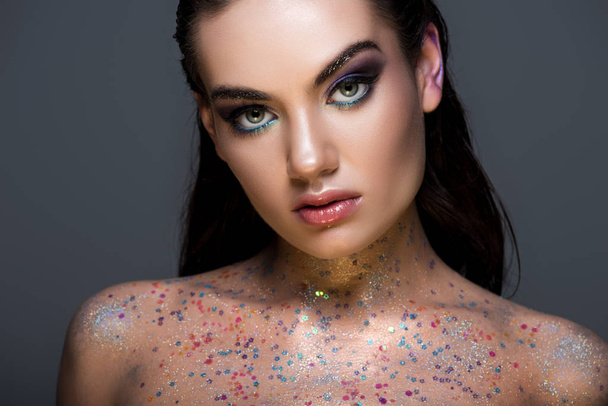 beautiful glamorous young model posing with glitter on body and looking at camera, isolated on grey - Photo, Image