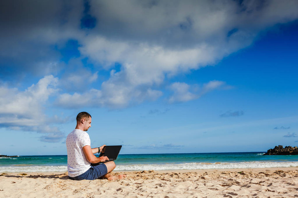 Young man with laptop working on the sand beach - Foto, imagen
