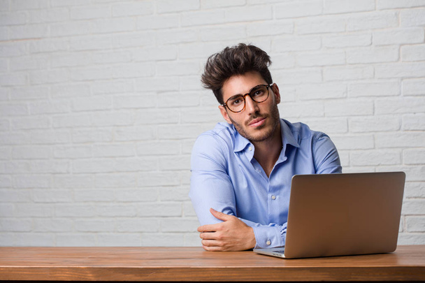Young business man sitting and working on a laptop cheerful and with a big smile, confident, friendly and sincere, expressing positivity and success - Photo, Image