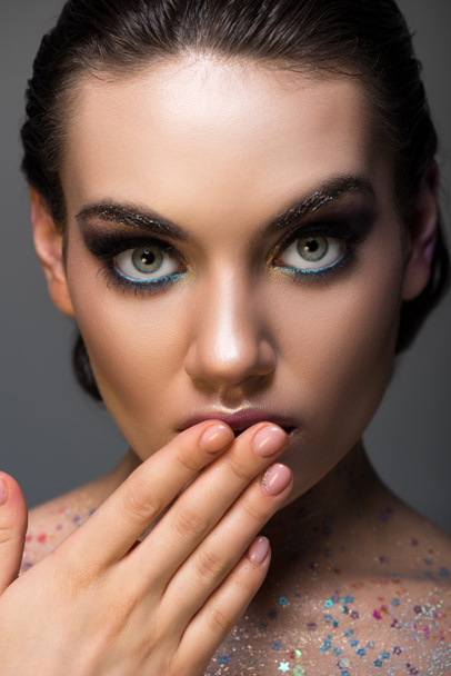 shocked glamorous girl posing with makeup and glitter on body, isolated on grey - Foto, Imagem