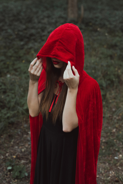 misztikus nő piros köpenye és a motorháztető, sötét erdőben - Fotó, kép