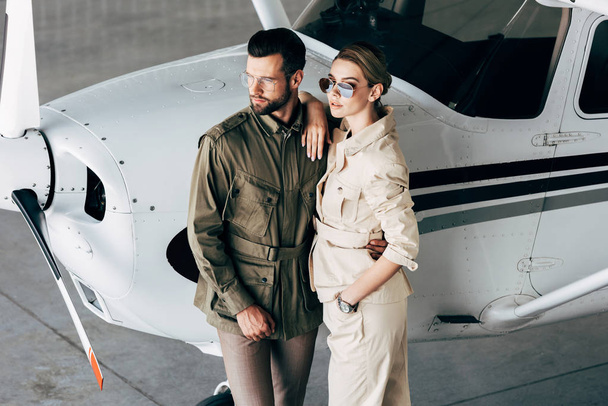 visão de ângulo alto de par jovem na moda em jaquetas elegantes que estão perto do avião
  - Foto, Imagem