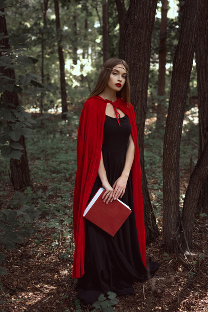 schönes Mädchen in rotem Mantel mit Zauberbuch im Wald - Foto, Bild