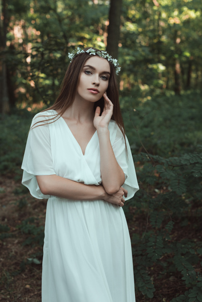 attractive young woman posing in stylish dress and floral wreath in forest - Photo, Image