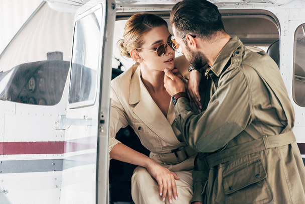 stylish young couple in jackets looking at each other near airplane  - Photo, Image
