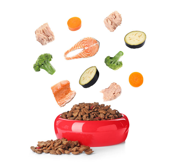 Ingredientes frescos que caen en un tazón con comida seca para mascotas para gatos y perros sobre fondo blanco
 - Foto, imagen