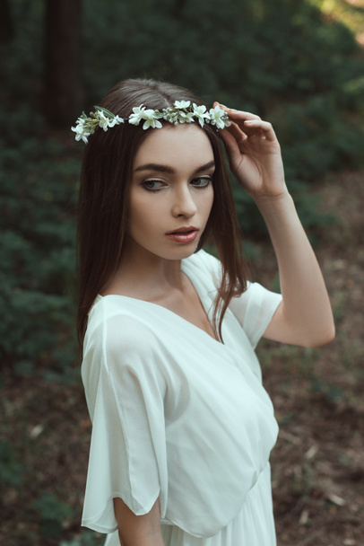 young woman posing in white dress and floral wreath in forest - Foto, Bild