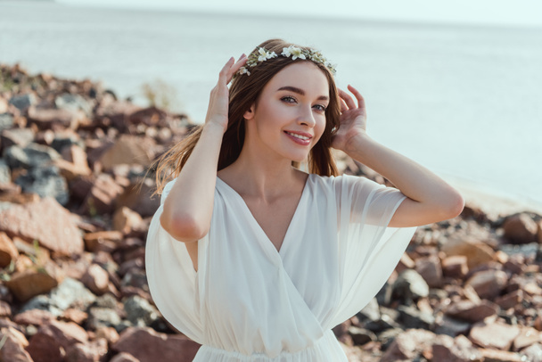 happy girl posing in white dress and wreath on rocky beach - Photo, Image