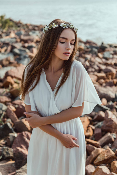 beautiful young tender woman posing in floral wreath on rocky beach - Valokuva, kuva