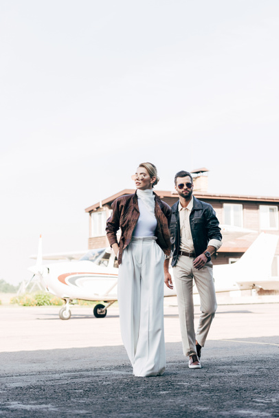 jeune couple élégant en lunettes de soleil et vestes en cuir marchant près de l'avion
 - Photo, image