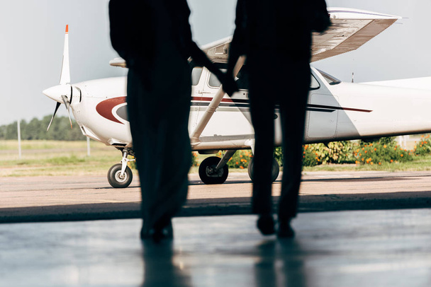 περικομμένη εικόνα σιλουέτες του νεαρό ζευγάρι κρατώντας τα χέρια και τα πόδια στο αεροπλάνο  - Φωτογραφία, εικόνα