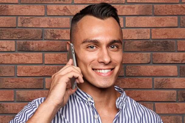 Young man talking on phone against brick wall - Фото, изображение