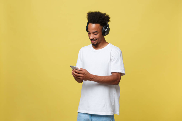 Młody czarny człowiek słuchania muzyki przez słuchawki. Na białym tle nad żółtym tle. - Zdjęcie, obraz