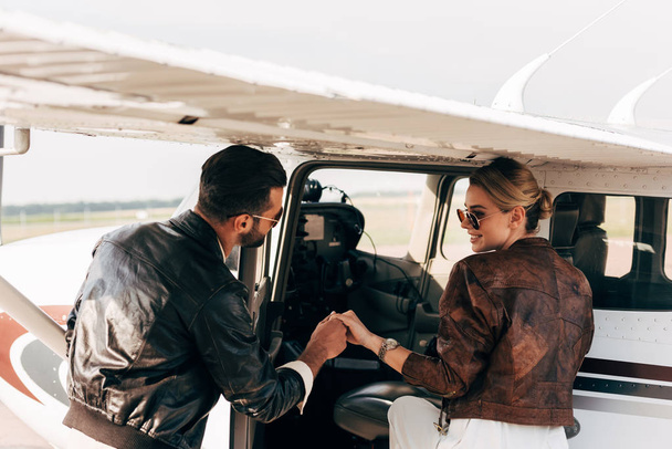 rear view of young man in leather jacket helping girlfriend boarding in airplane  - Фото, изображение