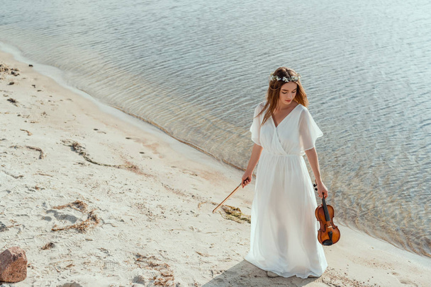 aantrekkelijk meisje in witte jurk bedrijf viool aan kust - Foto, afbeelding