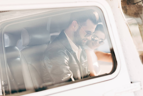 vista lateral del piloto masculino en gafas de sol y chaqueta de cuero con novia sentada cerca en cabina de avión
  - Foto, imagen