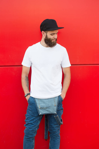 Hipster handsome male model with beard wearing white blank t-shirt and a baseball cap with space for your logo - Fotografie, Obrázek