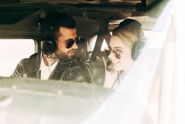 αρσενικό πιλότος στα ακουστικά και γυαλιά ηλίου, μιλώντας με τη φίλη στην καμπίνα του αεροπλάνου - Φωτογραφία, εικόνα