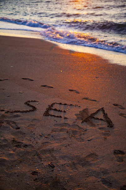 Beautiful sea at sunset. Word "sea" in the sand. Seascape. - 写真・画像