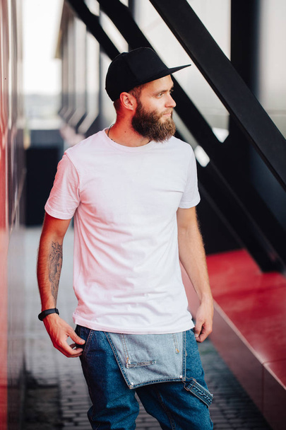 Hipster handsome male model with beard wearing white blank t-shirt and a baseball cap with space for your logo - Foto, immagini