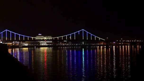 Iluminación nocturna en el puente, Hermoso puente por la noche iluminado reflectante luces paisaje urbano, Noche Tiempo Lapso escena del puente, Kiev puente peatonal sobre el río Dnepr bellamente iluminado por la noche y reflejado en el agua
 - Metraje, vídeo