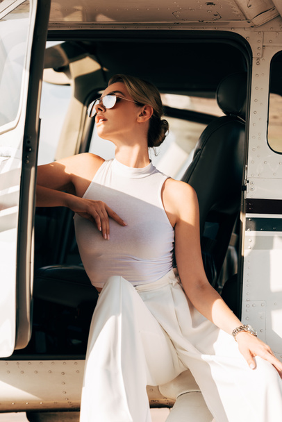 lage hoekmening van jonge vrouw in zonnebril zitten in de buurt van vliegtuig - Foto, afbeelding