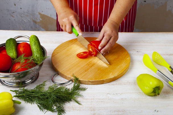 Frau in roter Schürze schneidet Gemüse für einen Salat auf einem Tisch in der Küche. Kochen. - Foto, Bild