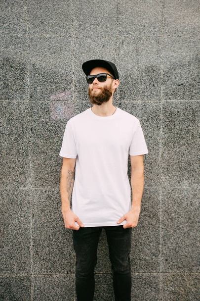 Hipster handsome male model with beard wearing white blank t-shirt and a baseball cap with space for your logo - Photo, Image