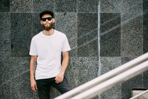 Hipster handsome male model with beard wearing white blank t-shirt and a baseball cap with space for your logo - Фото, зображення