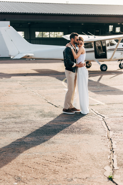 bel homme en veste en cuir et lunettes de soleil embrassant petite amie attrayante près de l'avion
 - Photo, image