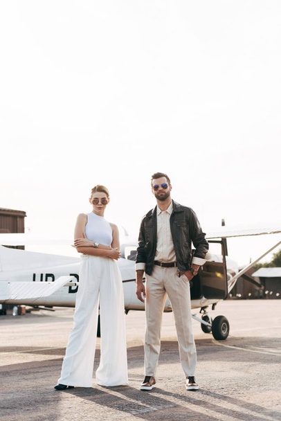 young fashionable couple in sunglasses posing near airplane  - Valokuva, kuva