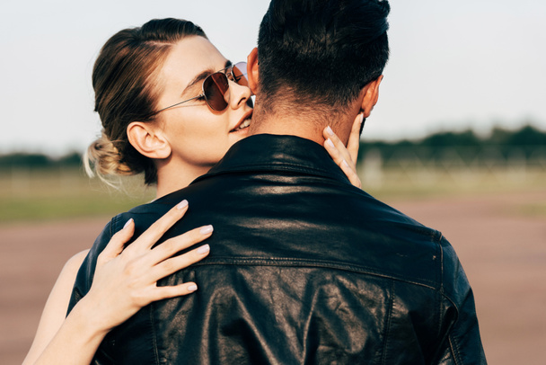 selective focus of beautiful smiling woman embracing boyfriend in leather jacket  - Foto, Imagen