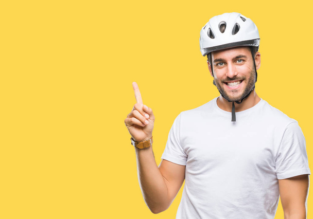 Mladý pohledný muž nosit ochrannou přilbu cyklista izolované pozadí s velkým úsměvem na tváři, rukou a prstu přejdete na straně při pohledu na fotoaparát. - Fotografie, Obrázek